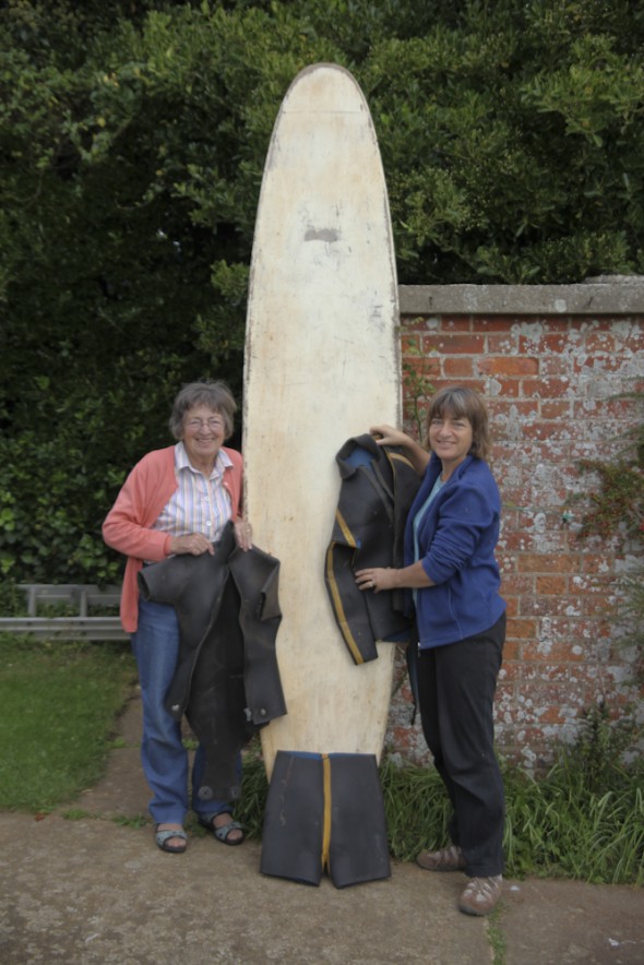 Betty & Sarah with wetsuits and surfboard